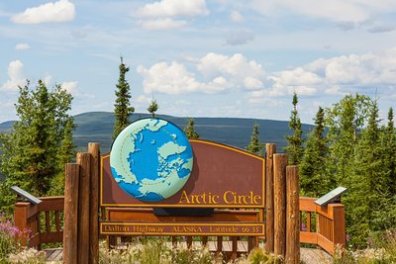 Sign marking the Arctic Circle with forest and cloudy sky in the background.