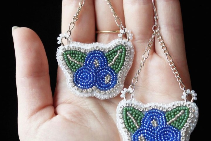 Hand holding beaded butterfly earrings with blue and green beads on a chain.