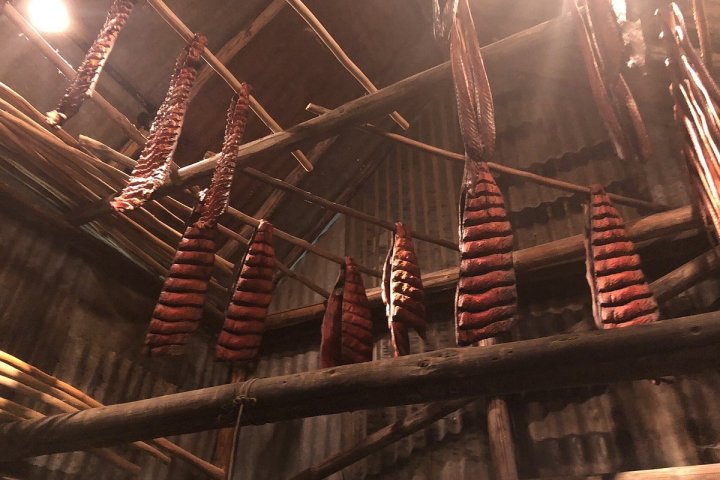 Strips of dried meat hanging from wooden rods in a dimly lit room.
