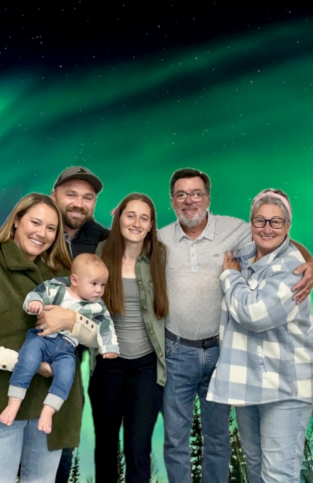 Family of six posing under green northern lights, including a baby.